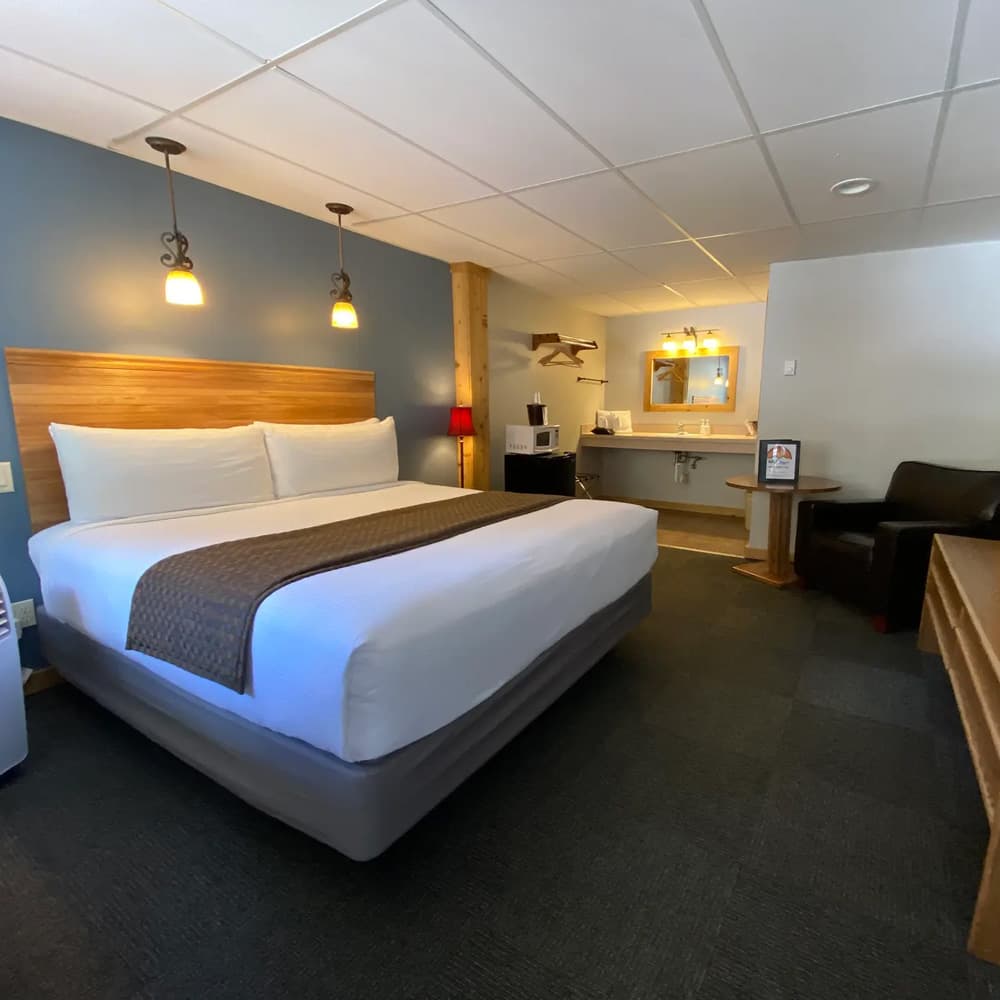 A neatly arranged hotel room with a large bed, wooden accents, and a small workspace.