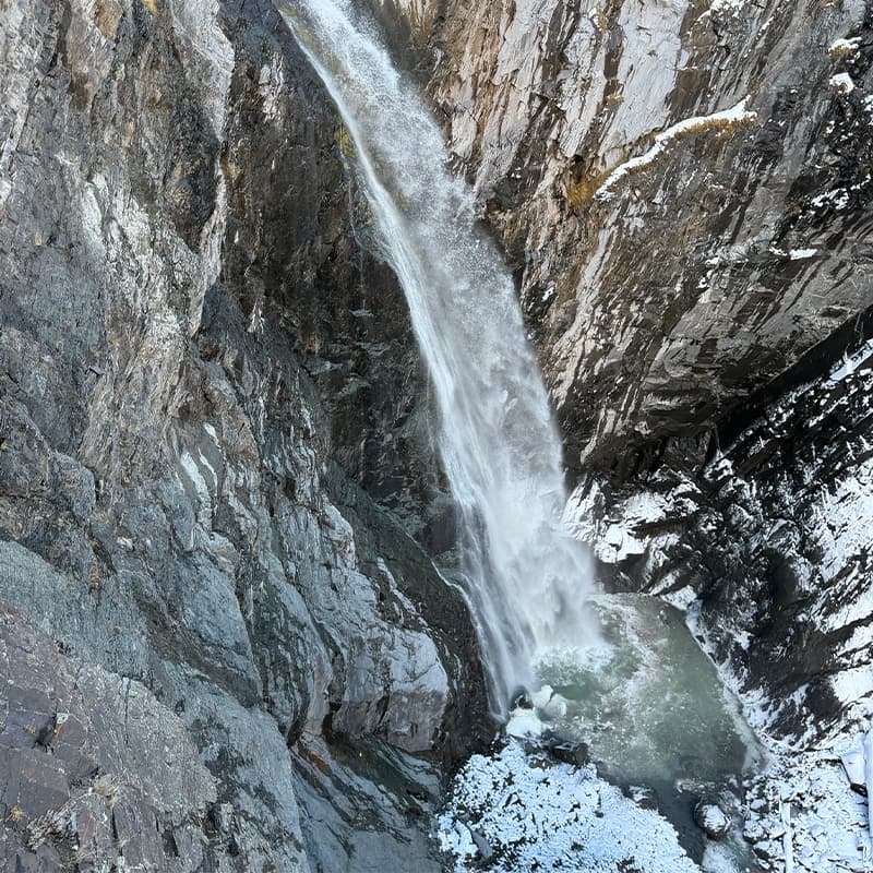 A waterfall cascades down rocky cliffs into a tranquil pool below, surrounded by snow.