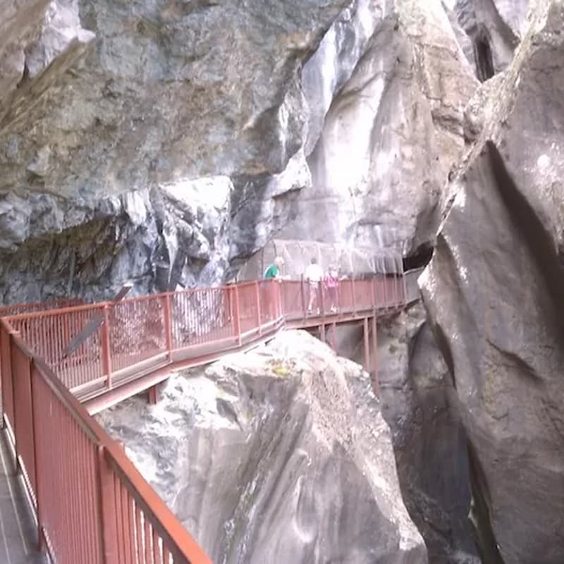 A narrow walkway with a railing runs through a rocky canyon.