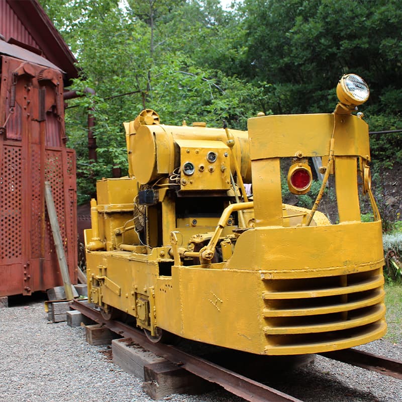 A vintage yellow railroad maintenance vehicle on tracks near a wooden structure.
