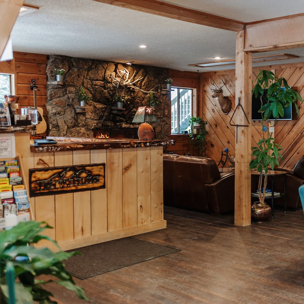 Cozy lodge reception area featuring wooden decor, a stone fireplace, and comfortable seating.